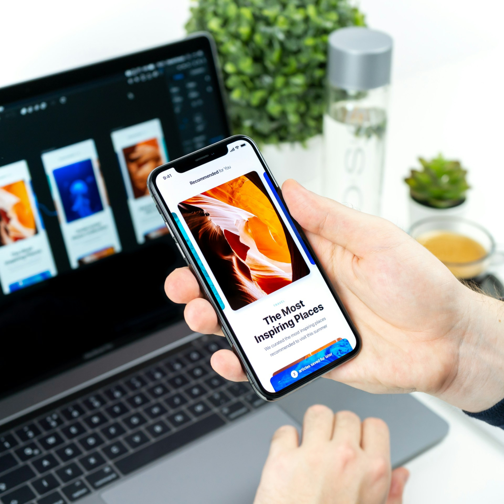 Une main qui tient un smartphone devant un ordinateur portable